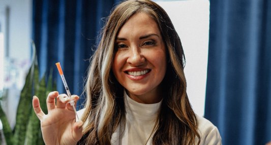 Smiling woman holding a syringe during a dermal filler consultation at a medical spa.